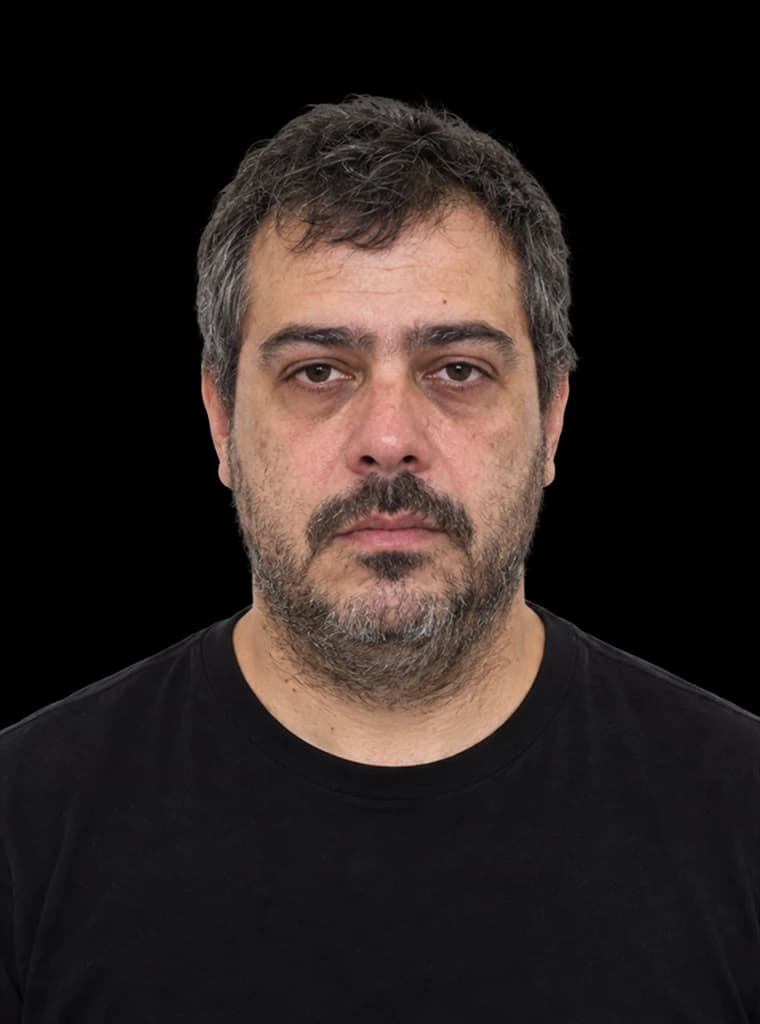 Homem de uns 40 anos, de camiseta preta, com cabelo sem corte, barba falhada, olheiras e expressão cansada.